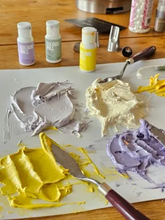 Palette knives and buttercream in yellow, lavender and cream tones on a worktable